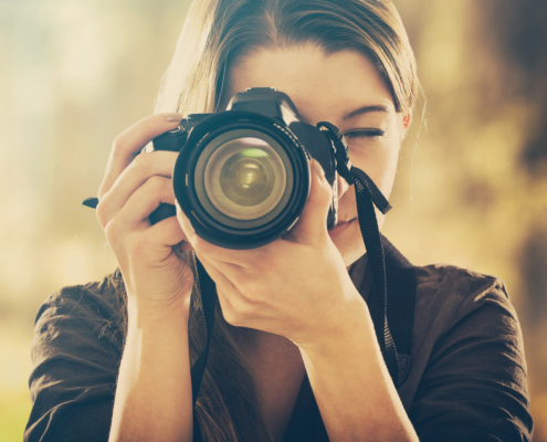 Portrait of a photographer covering her face with camera. Praxisübung zur Kameraeinstellung im Fotokurs Berlin